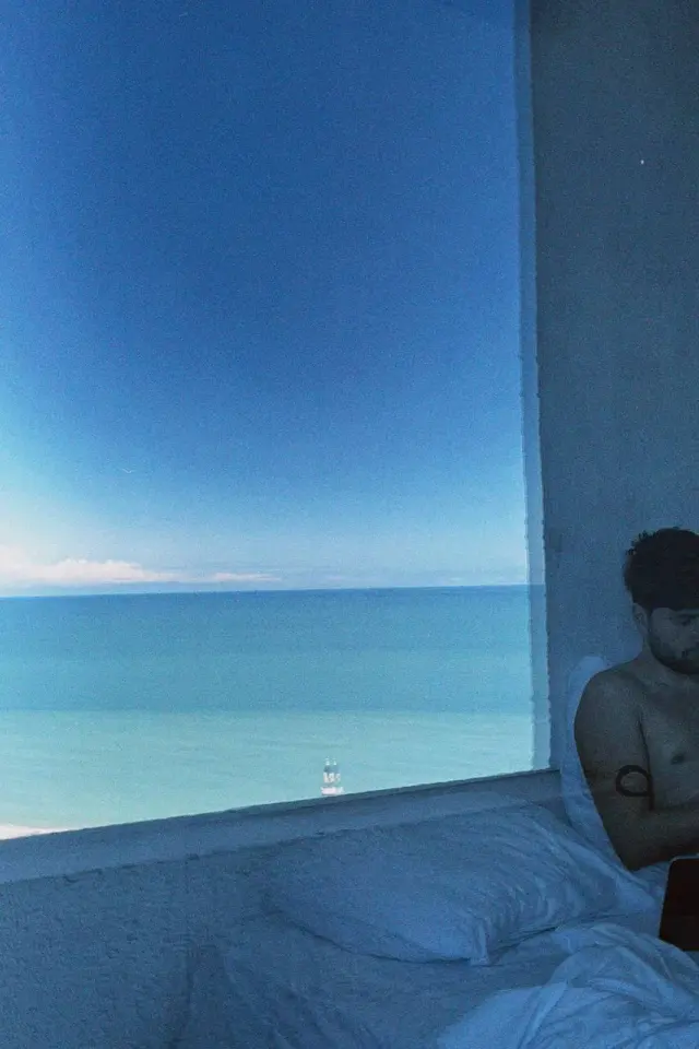 A sea view beside a bed and a person by the window