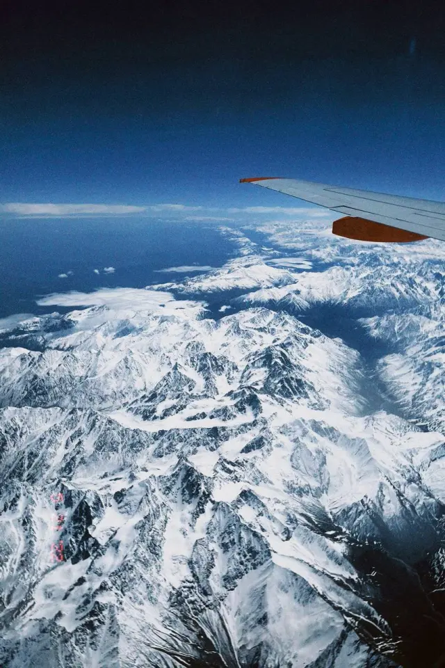 An airplane wing above snow-covered mountains
