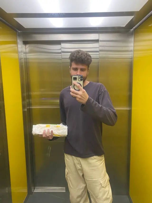 Alexey taking a mirror photo in an elevator while holding a wrapped meal