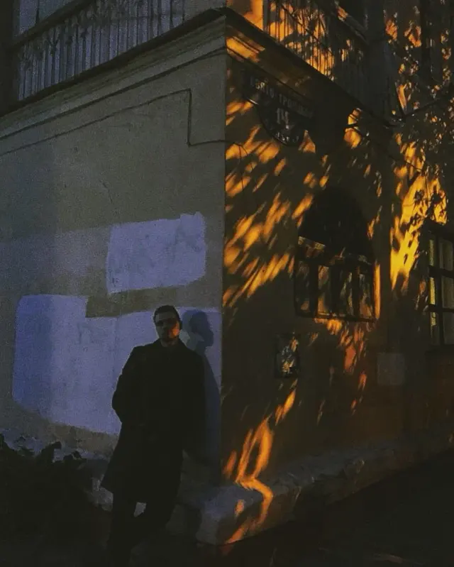 A person standing beside a sunlit wall