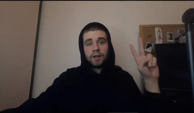 Alexey in a dark hoodie holding up two fingers